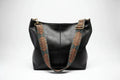 Black leather handbag with decorative brown straps on a white background